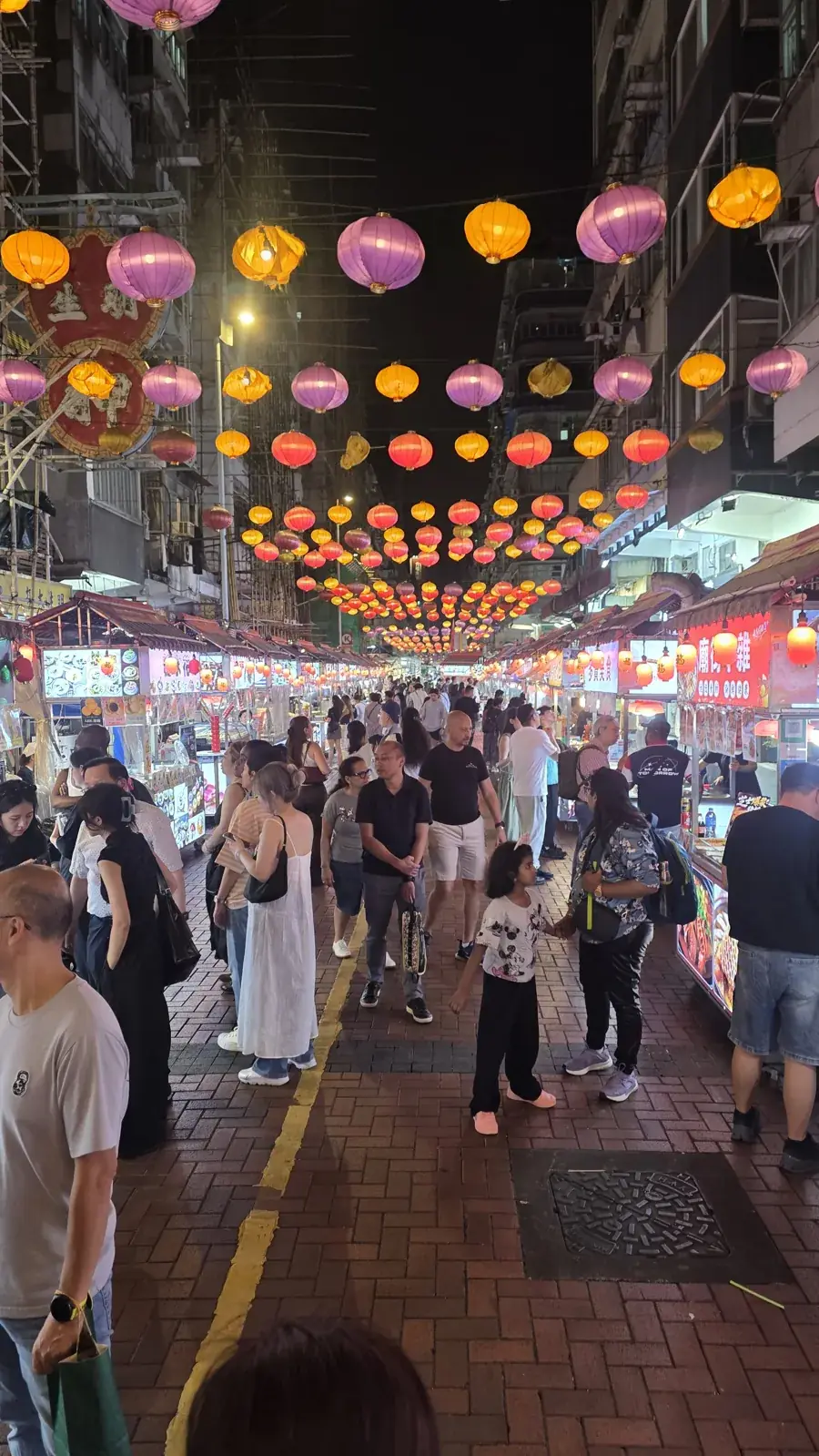 Colourful lanterns above market stalls and pedestrians on a Hong Kong street at night