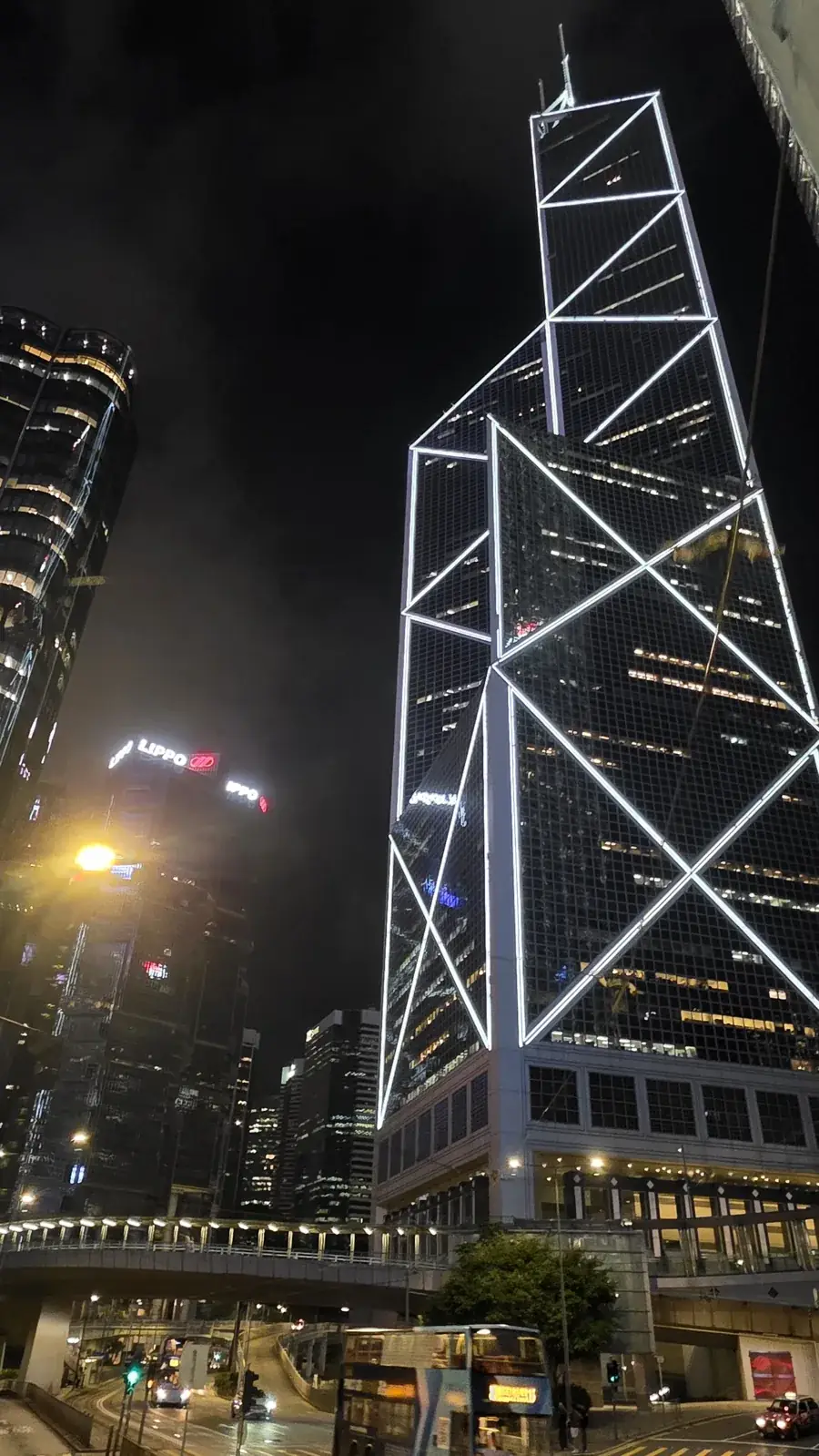The Bank of China Tower at night, with illuminated geometric lines and buses below