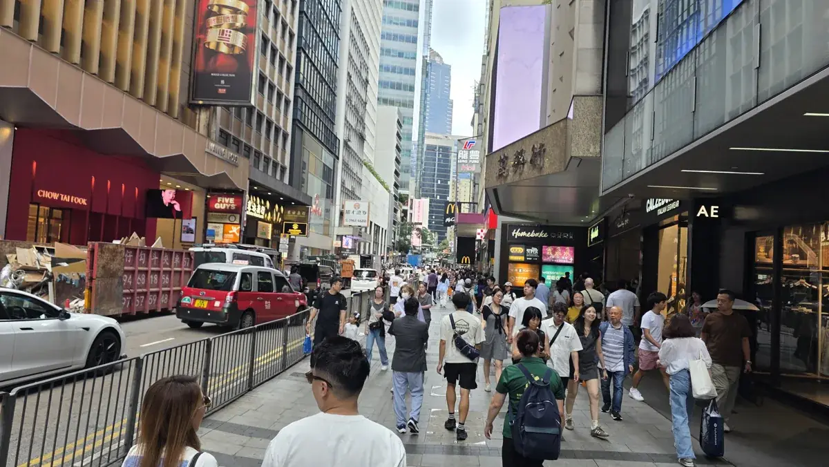 Pedestrians, a red taxi and shop signs along a busy commercial street in Hong Kong